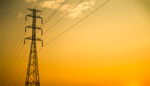 Electric transmission tower and power lines silhouetted against a yellow-orange sunset sky.